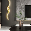 A modern minimalist gold LED wall lamp illuminates a textured gray wall in a contemporary interior setting.