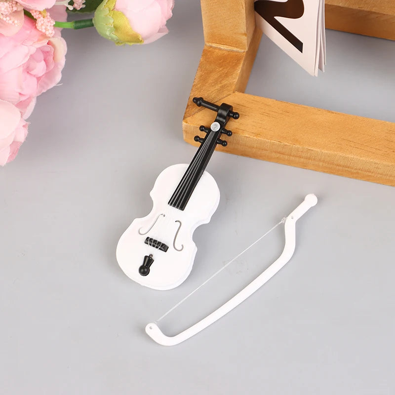 A white miniature piano with a black neck and bridge is displayed next to a wooden frame.
