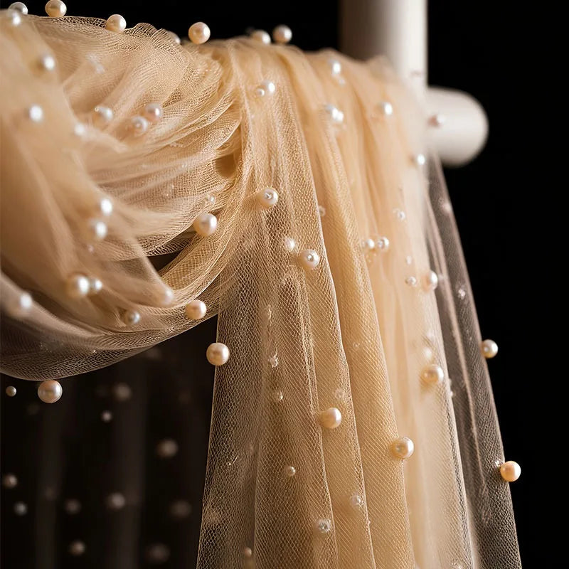 A sheer beige tulle fabric adorned with small pearls, draped elegantly.