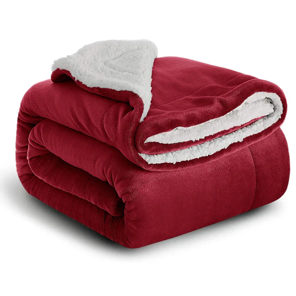 Manta de forro sherpa rojo intenso enrollada, mostrando un grueso ribete blanco y esponjoso.