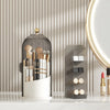 A gray rotating makeup brush holder with a dustproof lid and an acrylic storage stand on a white countertop.