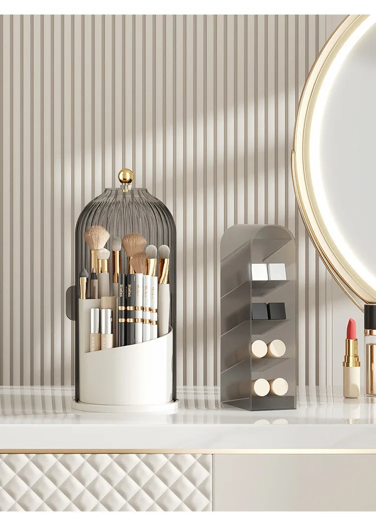 A gray rotating makeup brush holder with a dustproof lid and an acrylic storage stand on a white countertop.