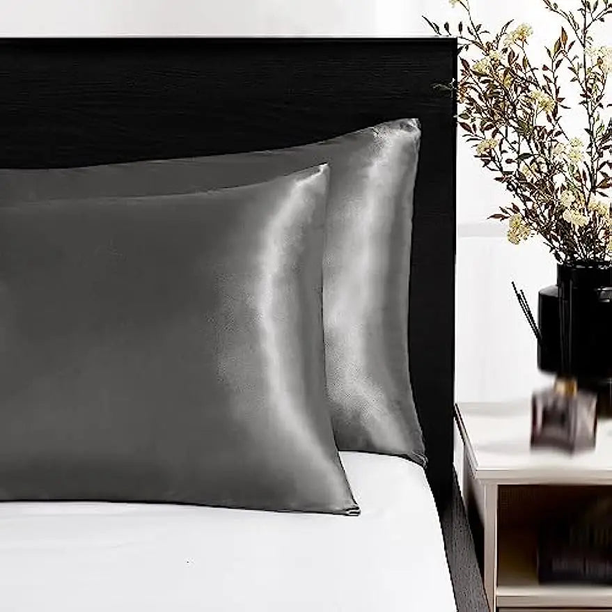 Un juego de fundas de almohada de seda satinada gris suave sobre una sábana blanca.
