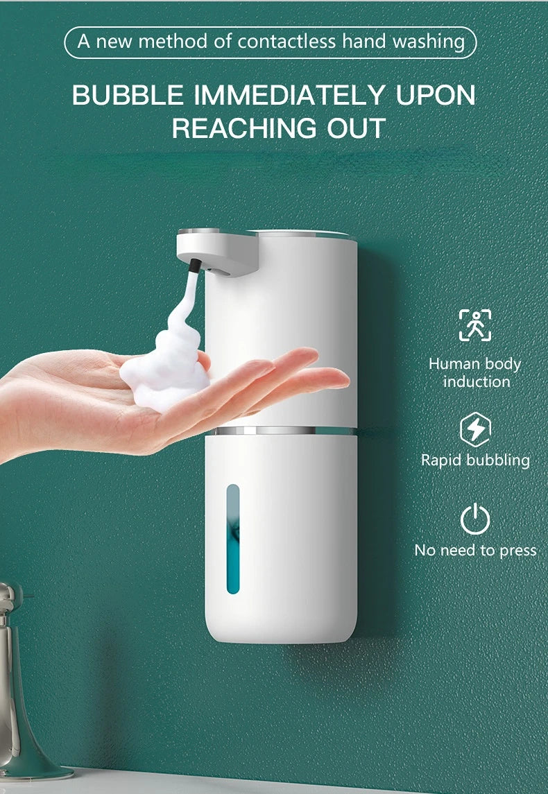 A hand is reaching out to a white touchless soap dispenser, which is producing a bubble immediately upon contact.