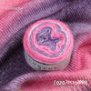 A roll of colorful gradient cake yarn showing pink and purple hues against a purple fabric background.
