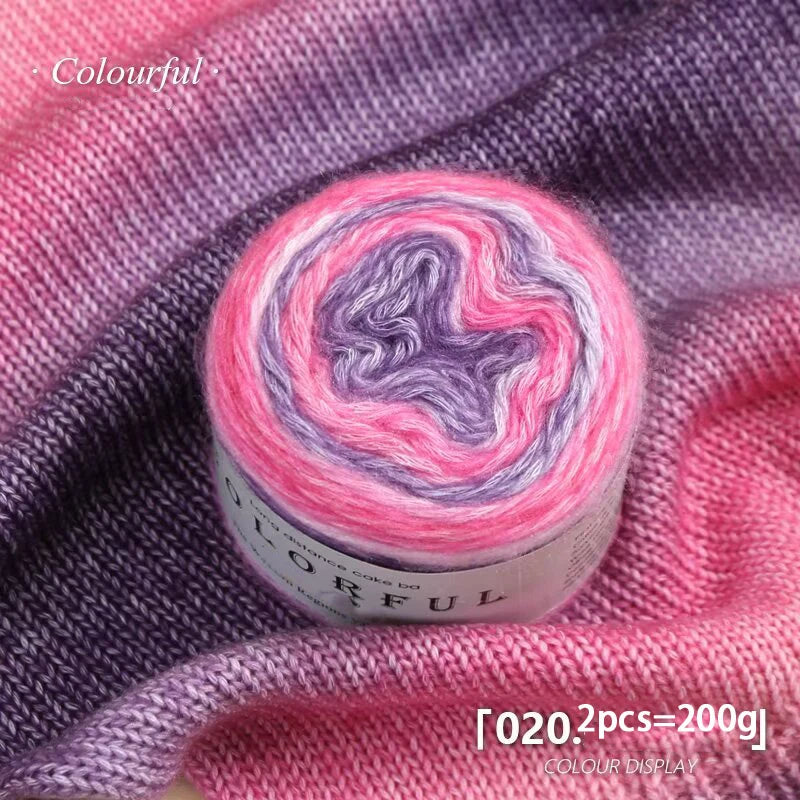 A roll of colorful gradient cake yarn showing pink and purple hues against a purple fabric background.