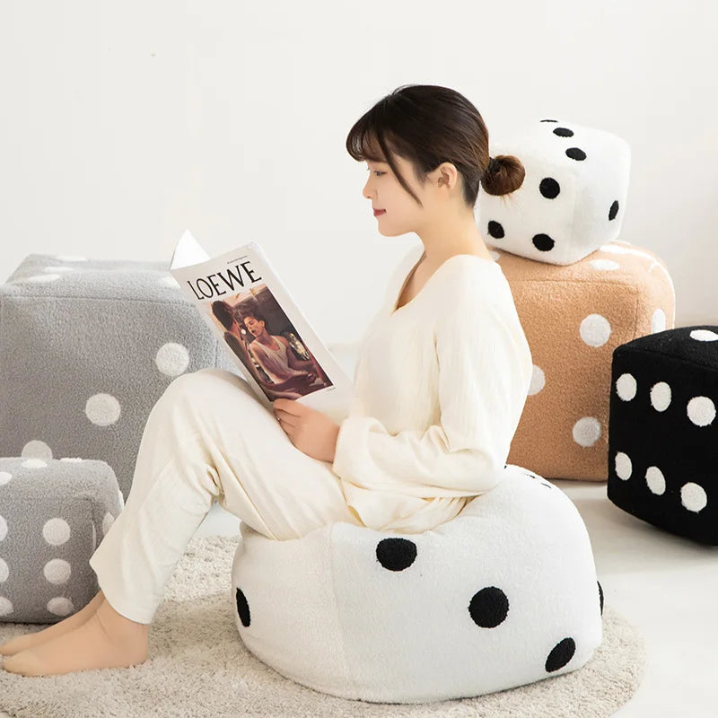 A woman sits on a white polka-dot plush cushion reading a magazine in a bright, indoor setting.