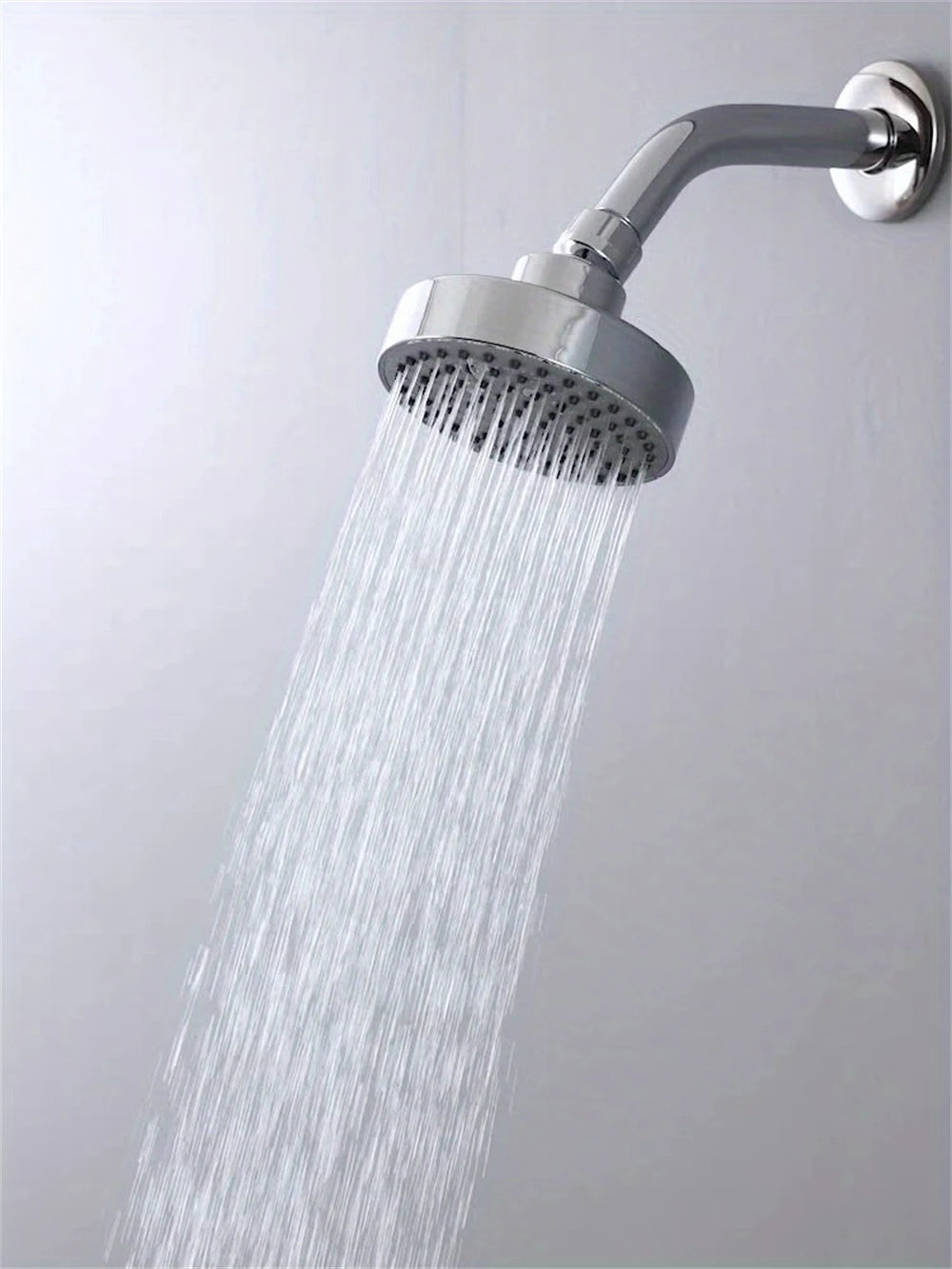 A matte black shower head is spraying a strong stream of water from a modern chrome faucet onto a white wall.