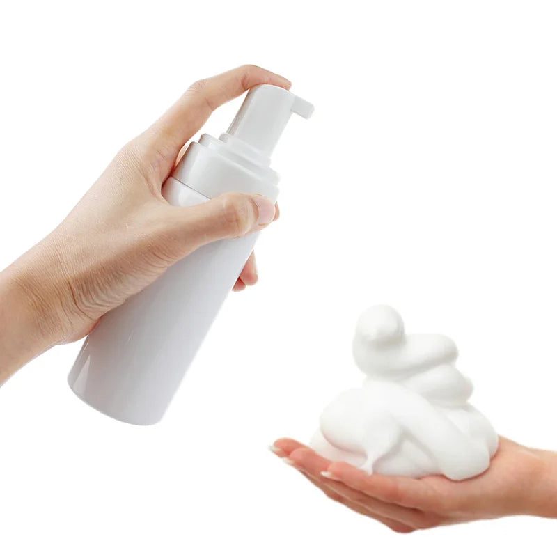A hand is holding a white refillable foaming soap dispenser bottle.