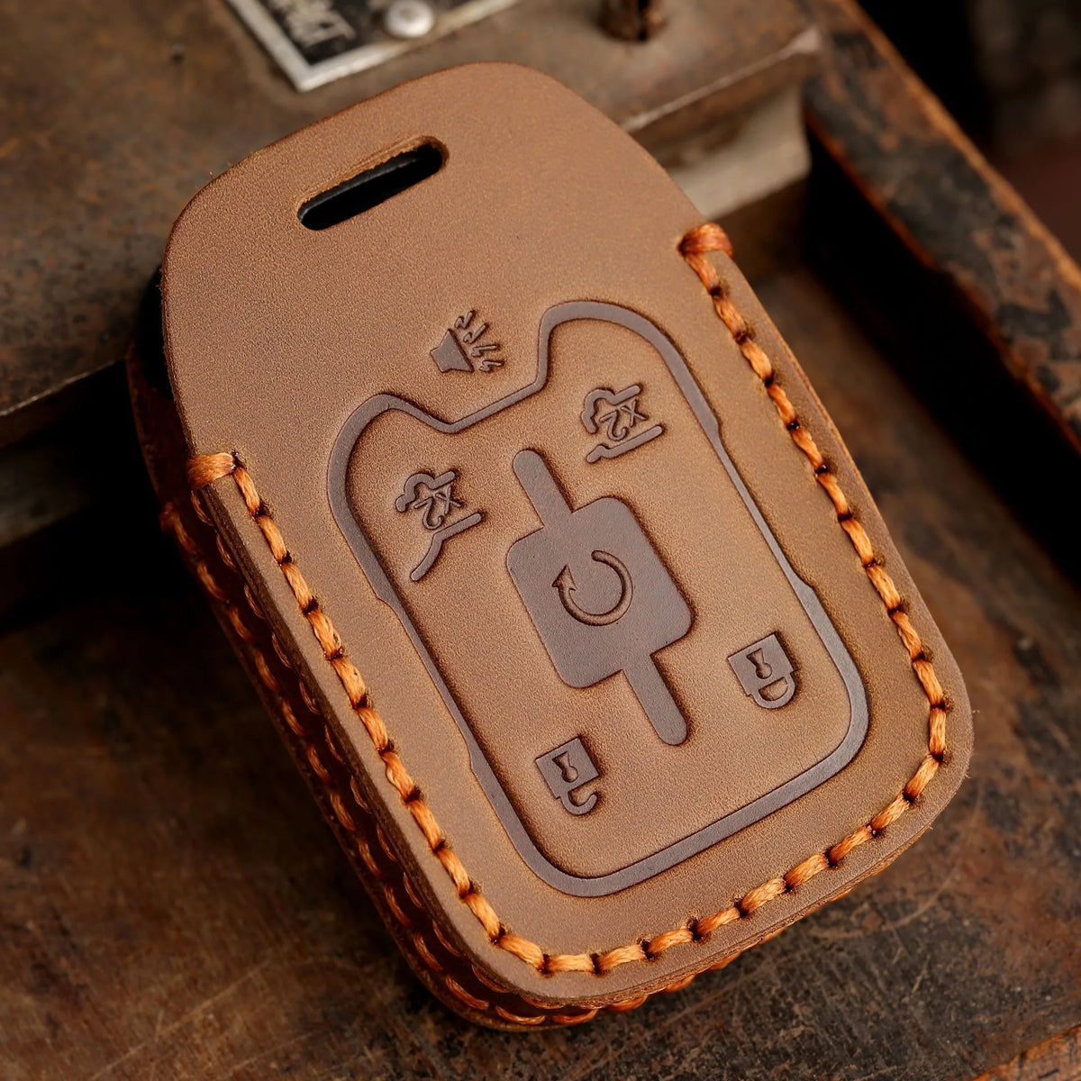A brown leather key fob case with embossed symbols for Chevrolet and GMC vehicles resting on a wooden surface.