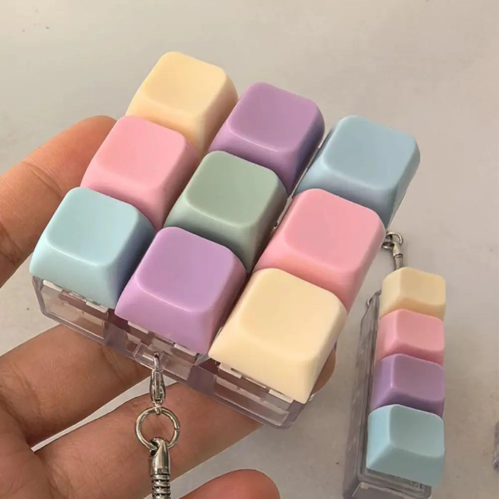 A hand holds a clear plastic case containing multiple pastel colored mechanical keyboard fidget keychains.