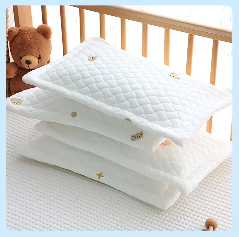 A stack of white quilted baby pillows with small gold star and bear embroidery resting on a white surface.