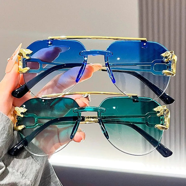 A hand holds a pair of gradient blue and green UV protection sunglasses against a light background.
