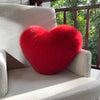 A bright red, fluffy heart-shaped throw pillow resting on a light-colored sofa.