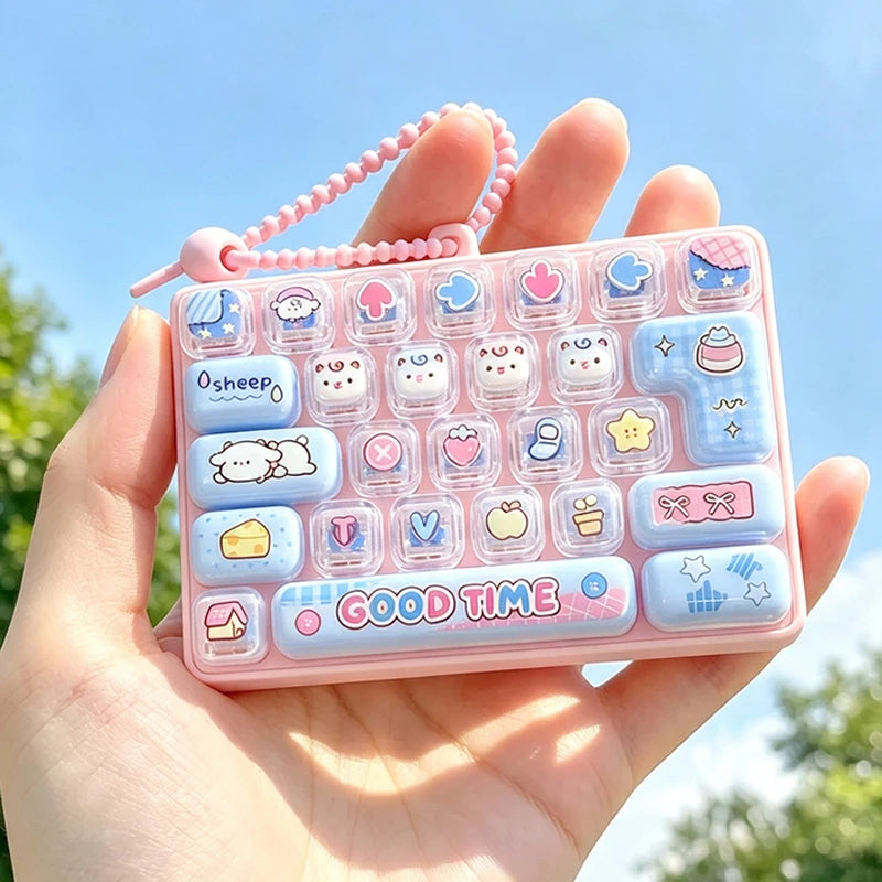A hand holds a pink acrylic keycap fidget keychain with various cartoon-themed buttons and a pink beaded chain against a brig