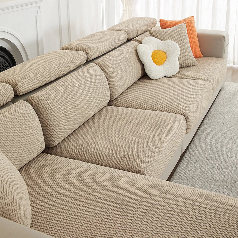 A beige jacquard elastic sofa slipcover with orange accent pillows on a light-colored sofa.