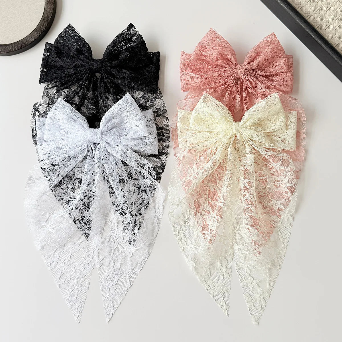 A pair of elegant lace bows in black, white, and pink are displayed on a light surface.