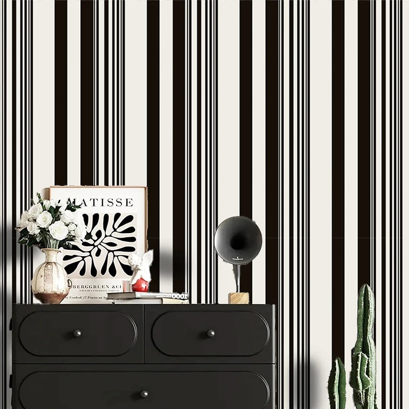 A black and white striped wallpaper roll is displayed next to a wooden box, some white flowers, and a green cactus.