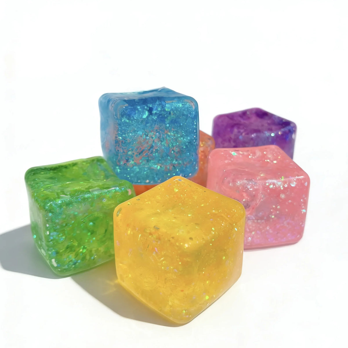 Eine Sammlung farbenfroher quadratischer Stressball-Fidget-Spielzeuge in Blau-, Grün-, Violett- und Pinktönen.