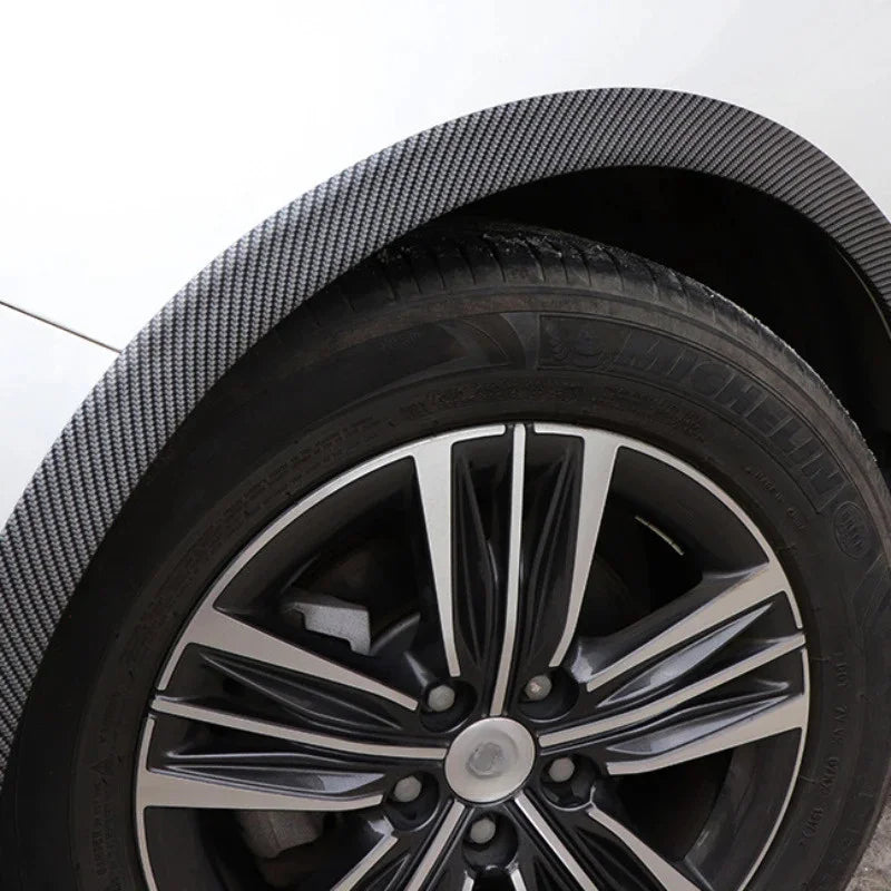 Close-up view of a black aftermarket wheel with a polished silver multi-spoke rim and textured carbon fiber-look fender trim.