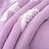 A close-up of a soft lavender plush jacquard throw blanket with white embroidered patterns.