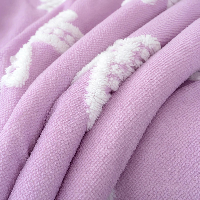 A close-up of a soft lavender plush jacquard throw blanket with white embroidered patterns.