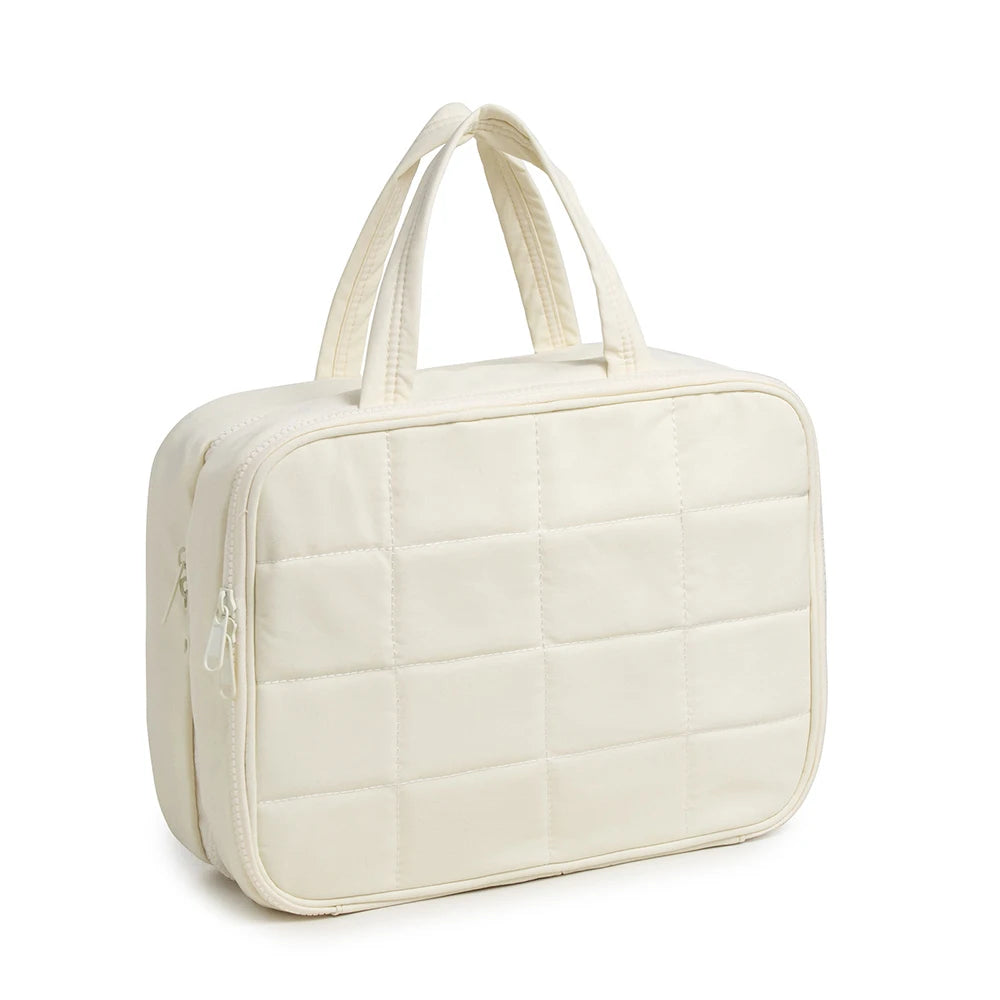 A cream-colored quilted portable hanging toiletry bag with fabric handles.