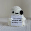 A handmade white crochet doll with black features holds a sign that reads Whatever you are get it off your chest and let them