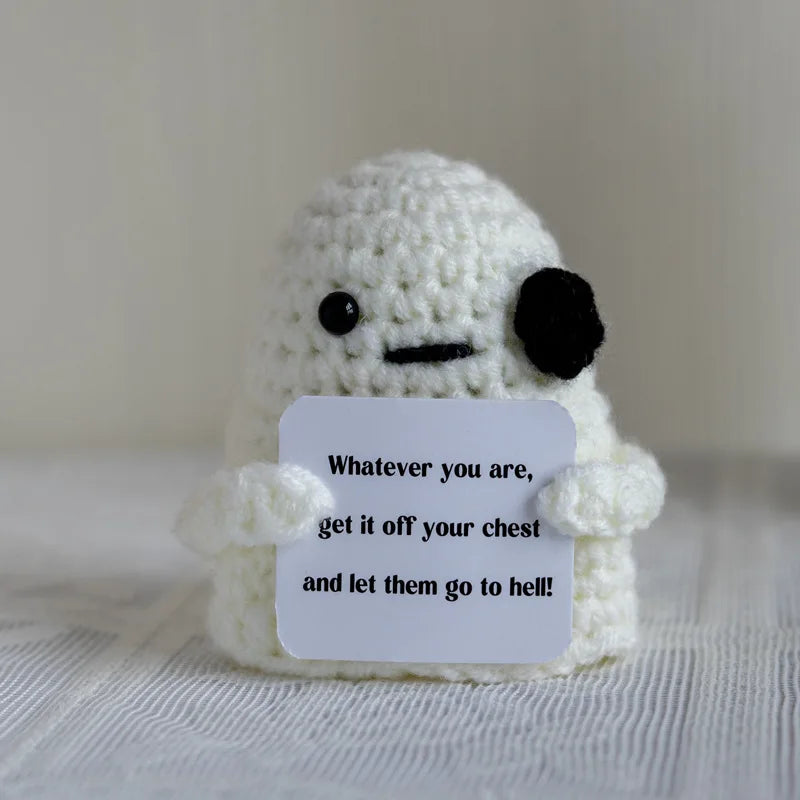 A handmade white crochet doll with black features holds a sign that reads Whatever you are get it off your chest and let them