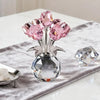 A crystal sculpture featuring a bouquet of pink and clear reflective roses displayed in a glass vase on a gray fabric.