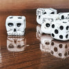A set of white skull dice for tabletop games and Halloween, displayed on a dark wooden surface.