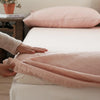 A close-up of a pink linen fitted sheet on a bed with a hand adjusting the fabric.