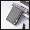A gray slim vertical leather wallet is shown resting on a white surface next to a Vogue Papers magazine.