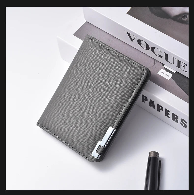 A gray slim vertical leather wallet is shown resting on a white surface next to a Vogue Papers magazine.