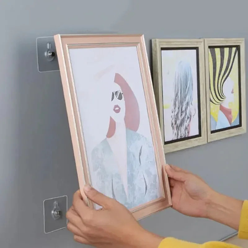 Hands holding a framed picture and two wooden frames with self-adhesive wall hooks.