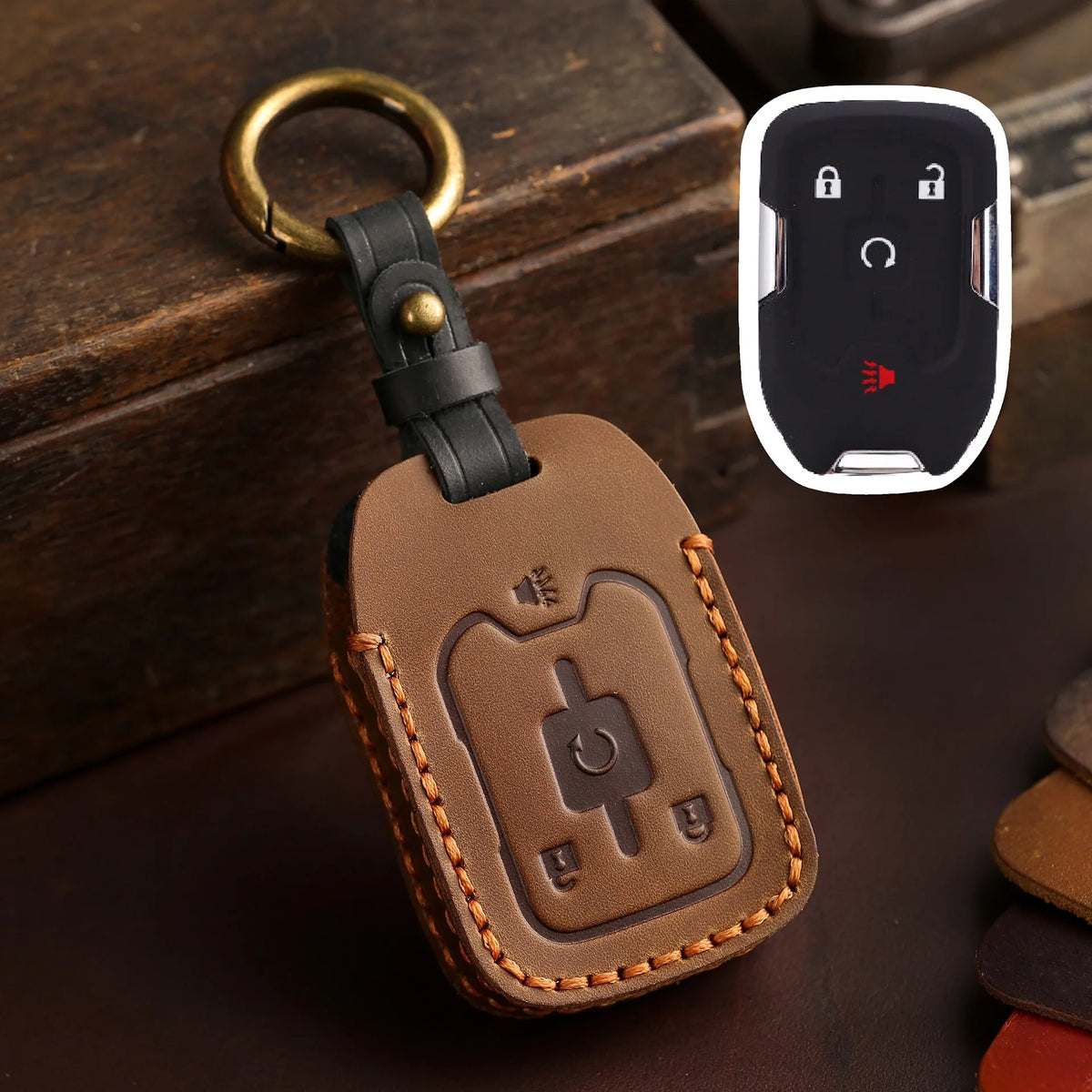 A brown leather key fob case with a brass ring attached, resting on a dark surface next to a white electronic device.