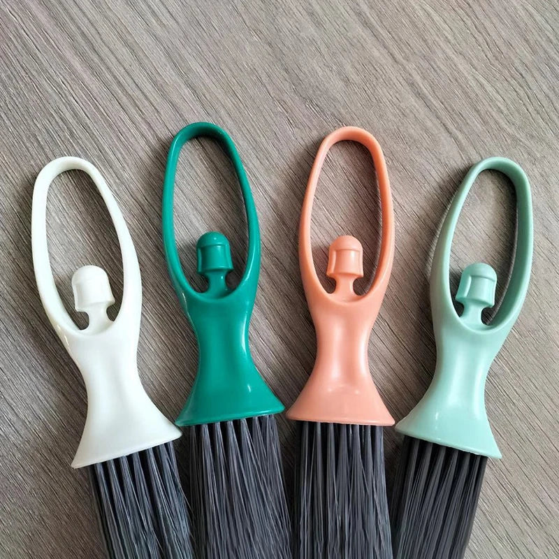 A set of compact mini brooms with black bristles and a green handle, shown against a gray background.