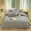 A light gray quilted duvet cover set with matching pillowcases displayed on a bed in a bright room.