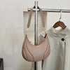 A light pink textured crossbody bag with a tan adjustable strap hanging on a metal rack.