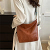 A woman wearing a white coat holds a brown leather shoulder bag with golden embroidery.