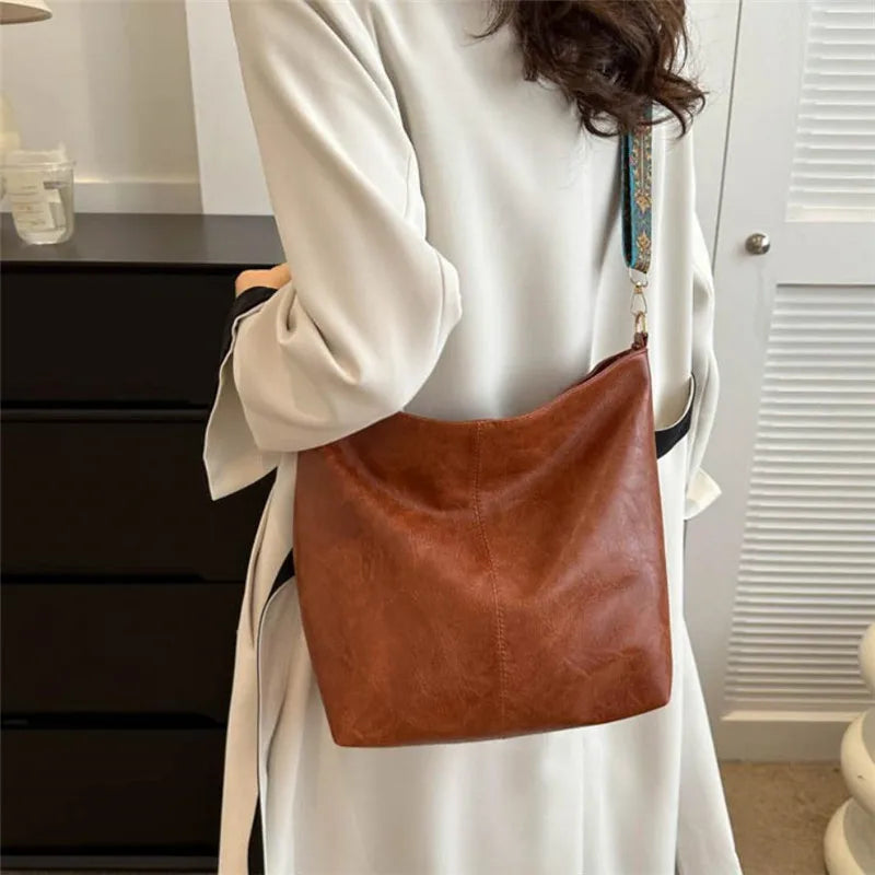 A woman wearing a white coat holds a brown leather shoulder bag with golden embroidery.