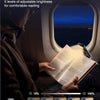 A person reads a book using a rechargeable clip-on LED book light in an airplane window.