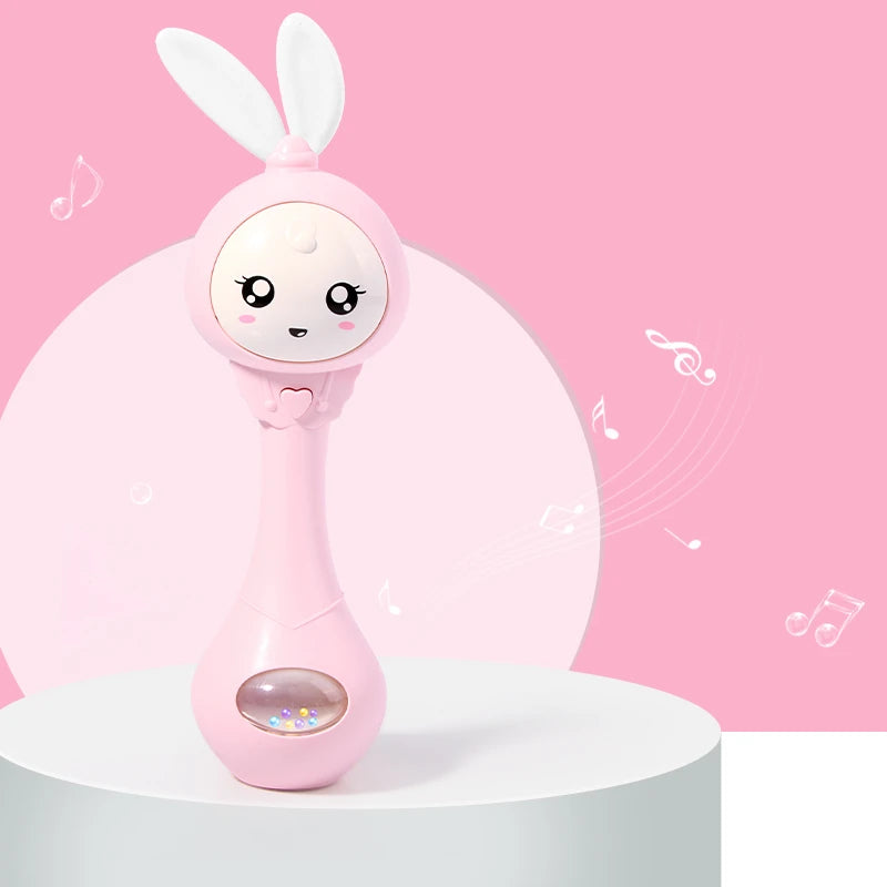 A pink musical rabbit rattle and teether toy is displayed on a white surface against a pink background.