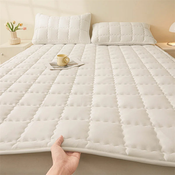 Gepolsterter weißer Matratzenaufsatz mit rutschfester Basis auf einem Bett, berührt von einer Hand.