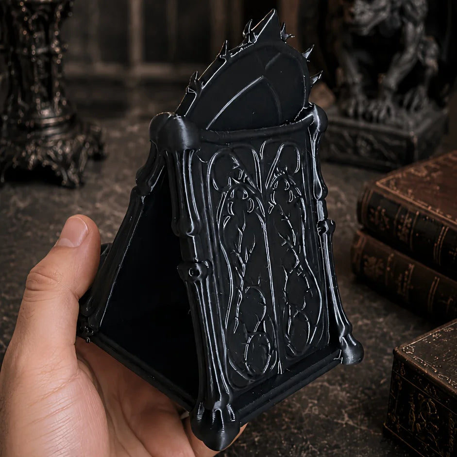 A hand holds an open black gothic skull phone stand with intricate thorn details.