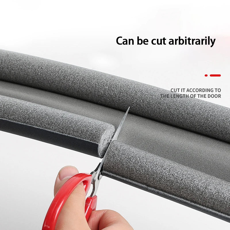 A hand cuts a flexible door bottom seal strip with scissors to fit the length of a door.