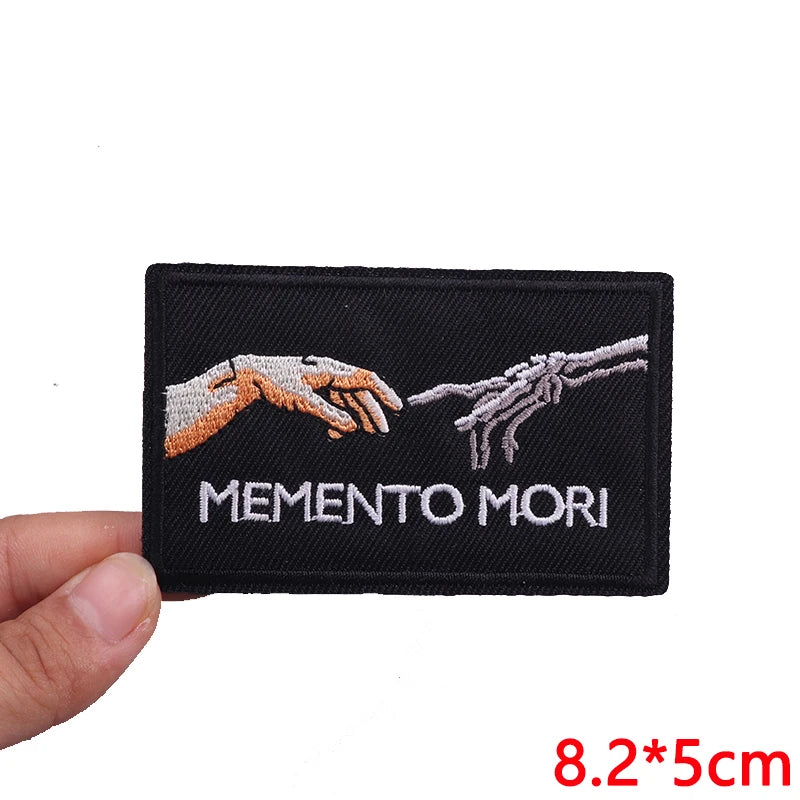 Black embroidered iron-on letter patch with the text MEMENTO MORI on it