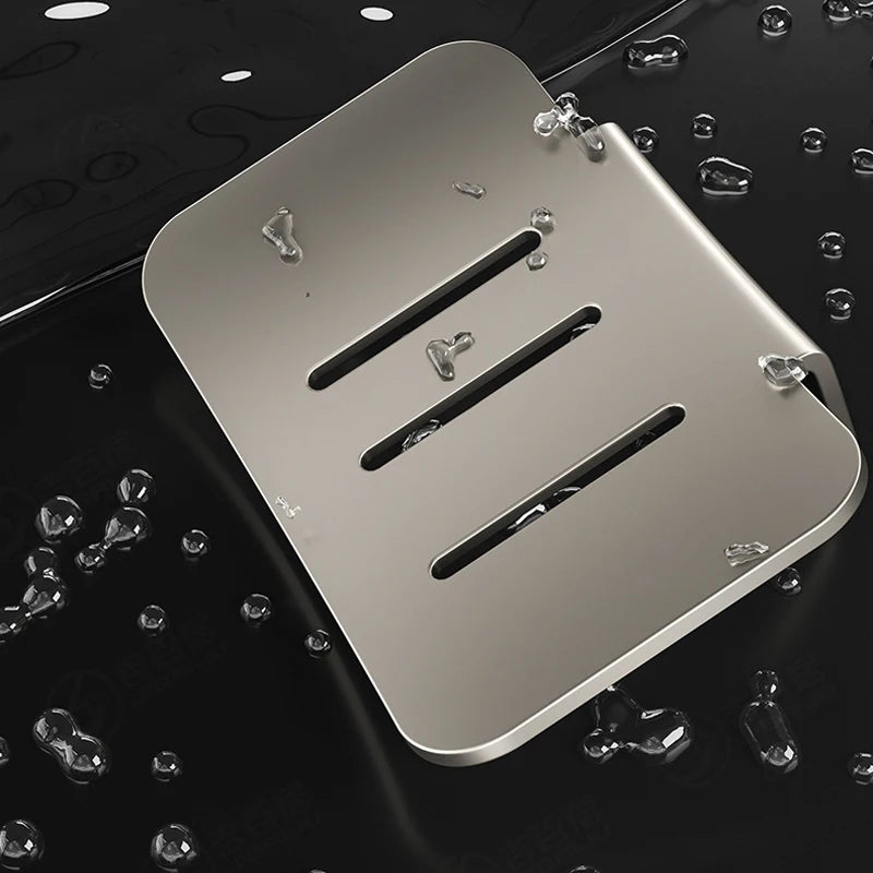 A silver aluminum wall-mounted soap dish with drainage slots is shown floating above a dark surface surrounded by water dropl
