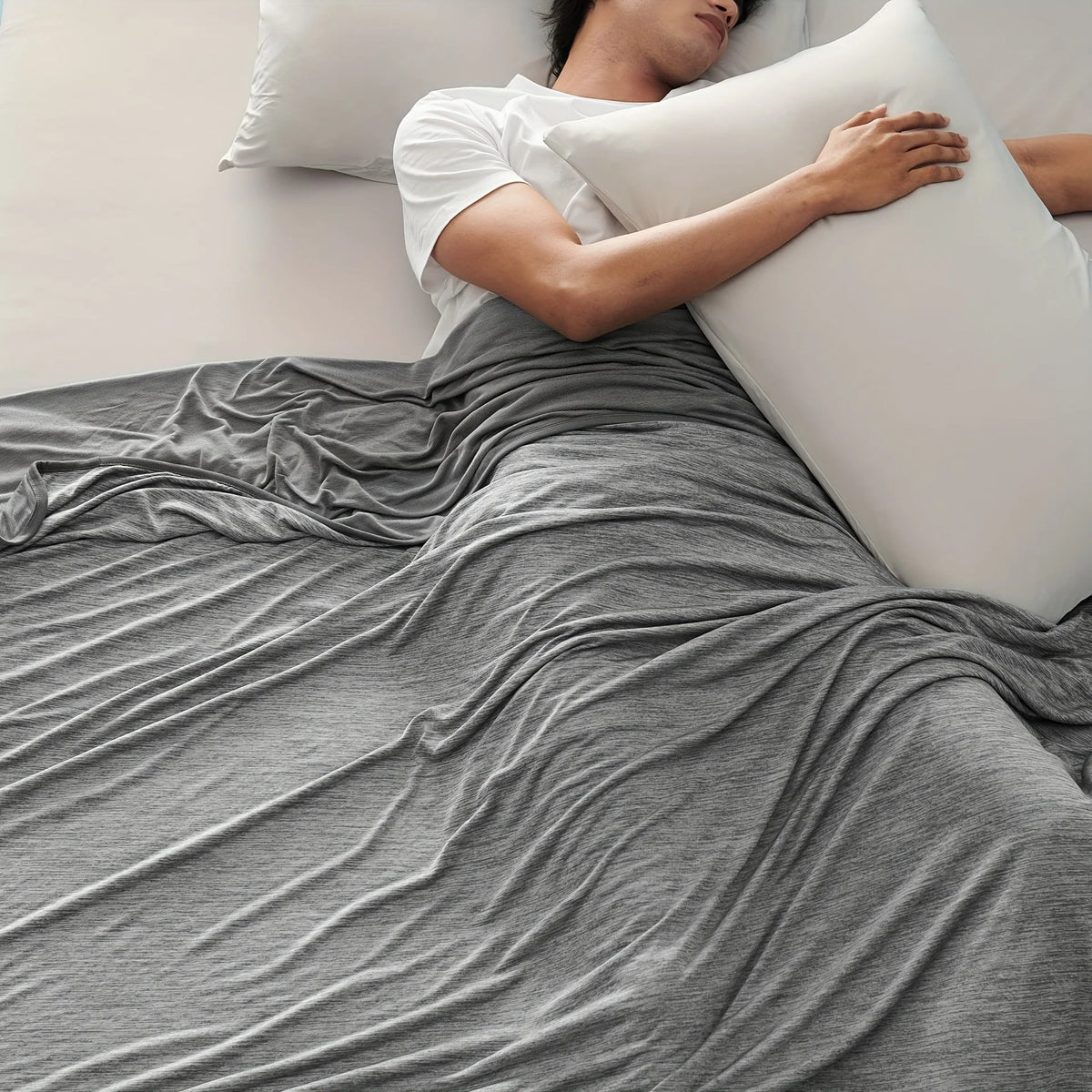 A person is lying down under a gray blanket with a white pillow, suggesting a cool-feel summer nap.