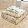 A stack of white and green lace-trimmed breathable summer duvets resting on a floral patterned bed.